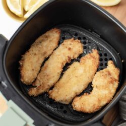 Golden crispy air fryer breaded chicken fillets on black air fryer basket.