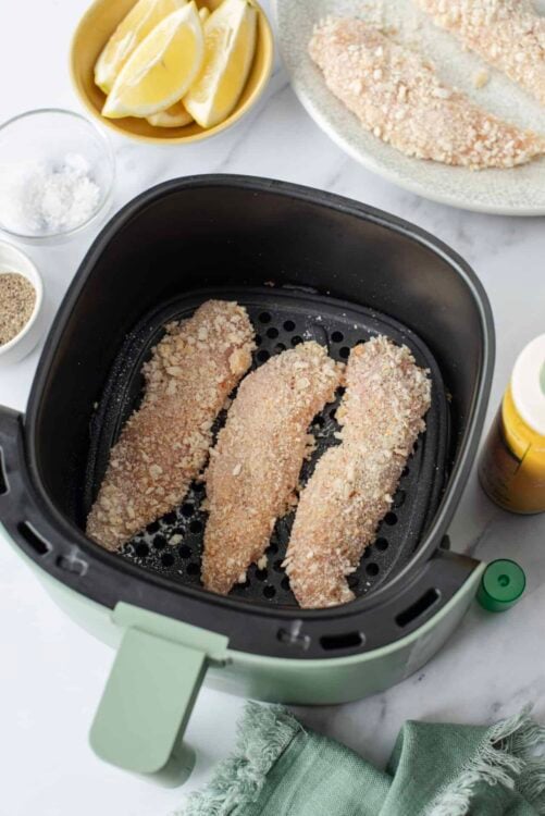 Crispy breaded chicken fillets cooking in an air fryer with lemon wedges in the background.