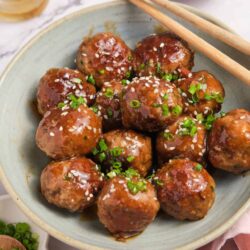 Savory teriyaki turkey meatballs with green onions and sesame seeds in a light green bowl.