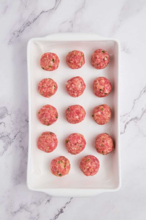 Seasoned meatball mixture ready to cook, top view on white marble background, homemade comfort food, recipe preparation, raw meatballs on white platter.