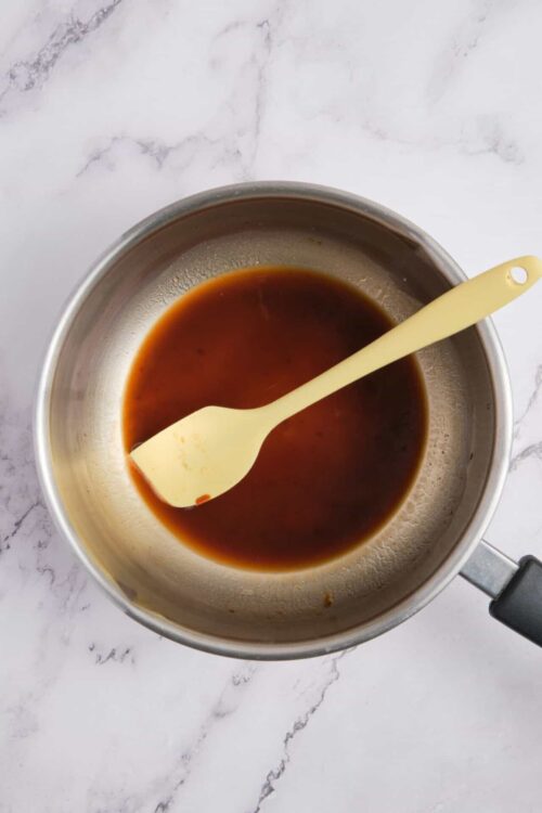 Caramel sauce in a saucepan with a spatula on a marble countertop.