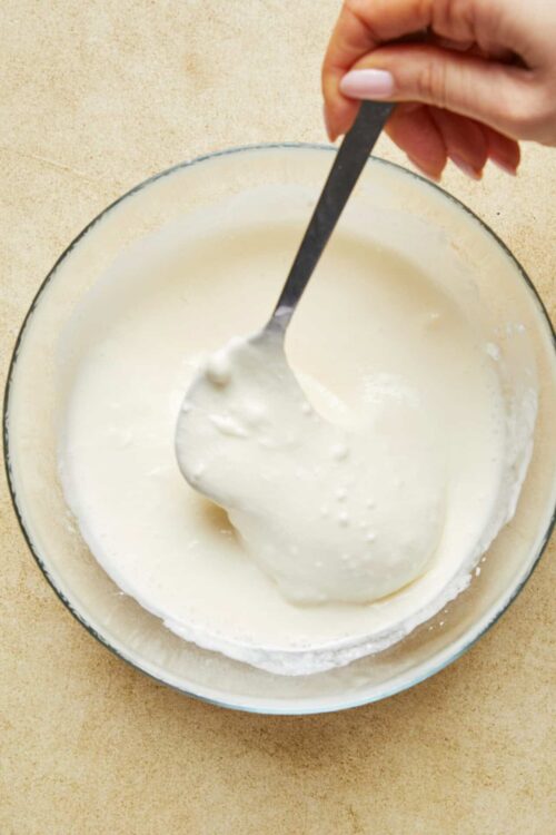Creamy homemade white sauce in a glass bowl with a spoon.
