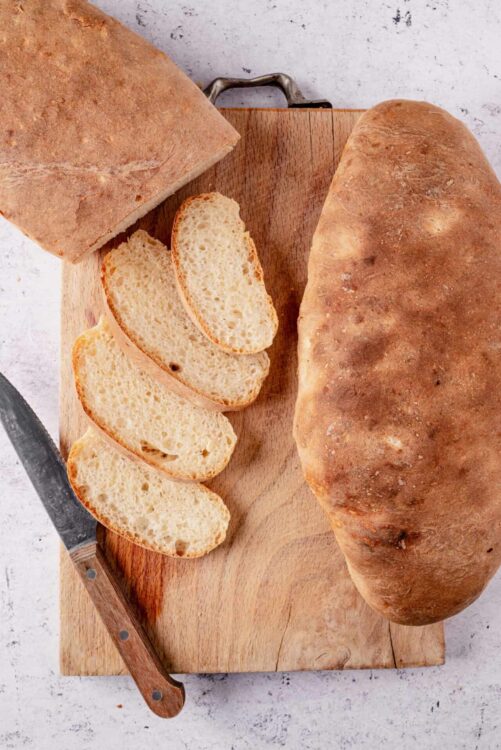 Fresh homemade Italian bread on a wooden cutting board with slices ready to serve.