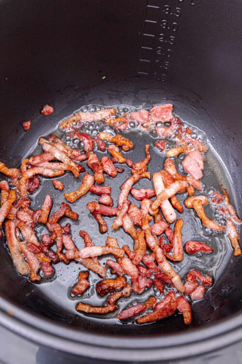 Crispy cooked bacon bits in a black air fryer basket.