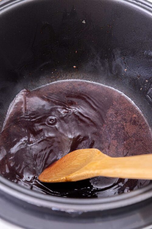 Baked bree chocolate sauce in slow cooker with wooden spoon.