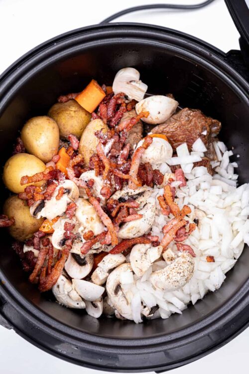 Crockpot ingredients with potatoes, bacon, mushrooms, onions, and beef for slow cooker beef stew.