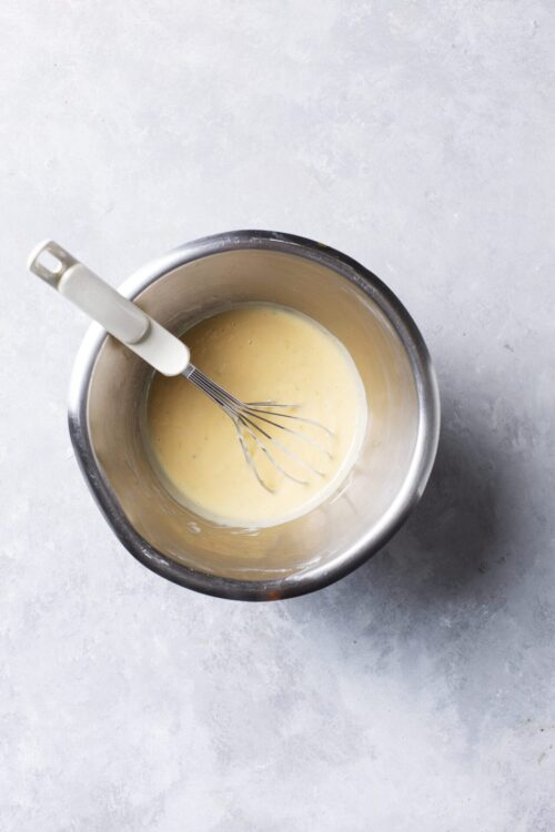 Whisked custard in stainless steel bowl for baking recipes.