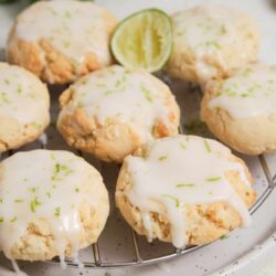 Lemon glaze scones with lime zest on a cooling rack, fresh lime halves in background.