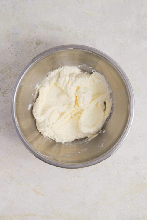 Cream cheese frosting in a stainless steel mixing bowl, ready for cake decorating.
