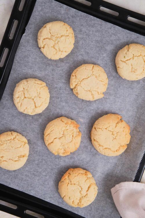 Freshly baked lemon cookies cooling on a baking sheet.