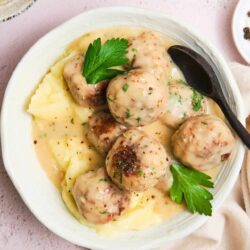 Creamy Swedish meatballs with mashed potatoes and gravy on white plate.