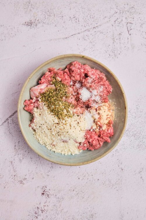 Fresh ground meat with herbs and spices in a ceramic bowl for baking or cooking recipes.