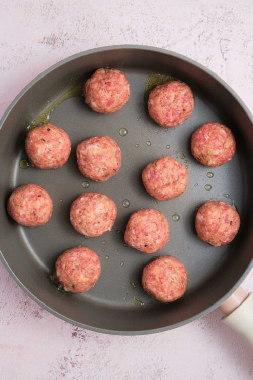 Minced meat mixture forming meatballs in a skillet for baked meatball recipe.
