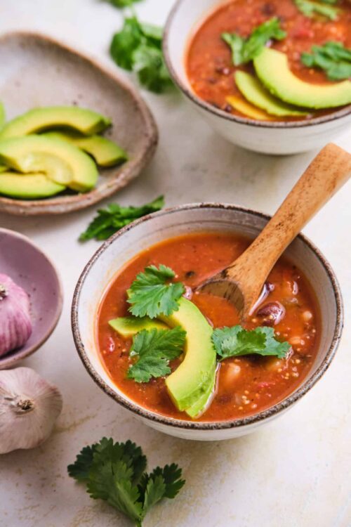 Creamy tomato soup with avocado and cilantro garnishes, served in rustic bowls with fresh ingredients.