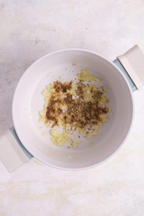 Minced garlic, dried herbs, and seasonings in a white clay pot for savory cooking.