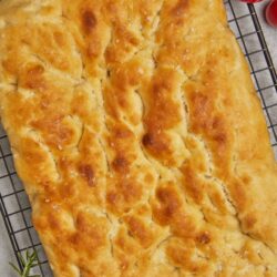Golden baked cheesy garlic bread on cooling rack, fresh tomatoes nearby.