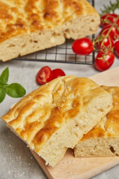 Fluffy cheesy garlic bread loaf on a wooden board with cherry tomatoes and fresh basil.