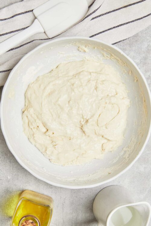 Creamy homemade bread dough in a white mixing bowl for baking recipes.
