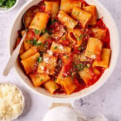 Pasta with tomato sauce and grated cheese, served in a white bowl with fresh herbs.