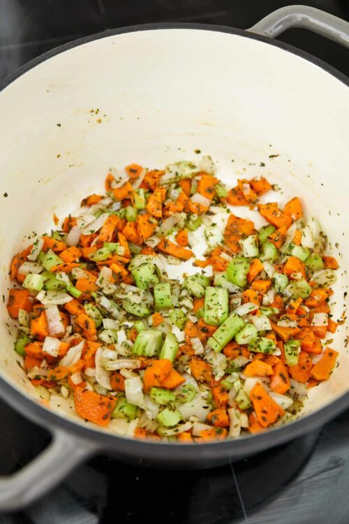 Sautéed vegetables in a cast iron skillet with herbs, including carrots, celery, and onions.