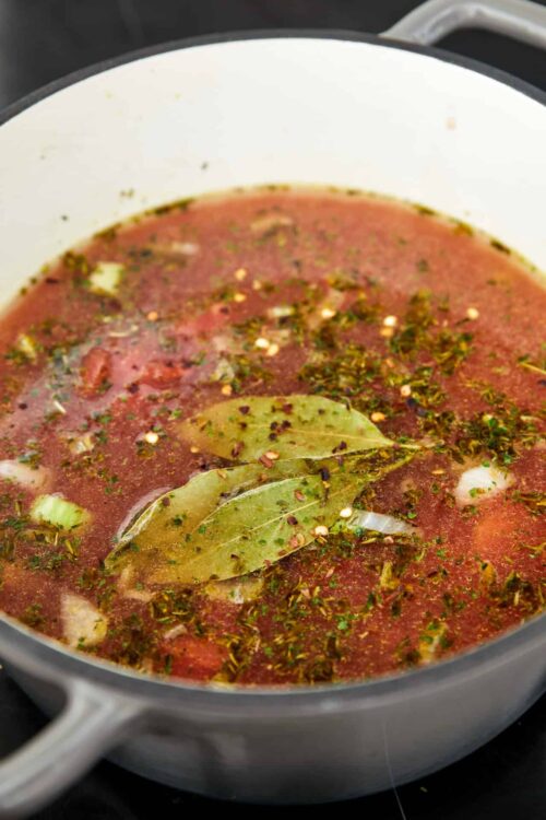 Flavorful beef broth with bay leaves and herbs simmering in a white pot.