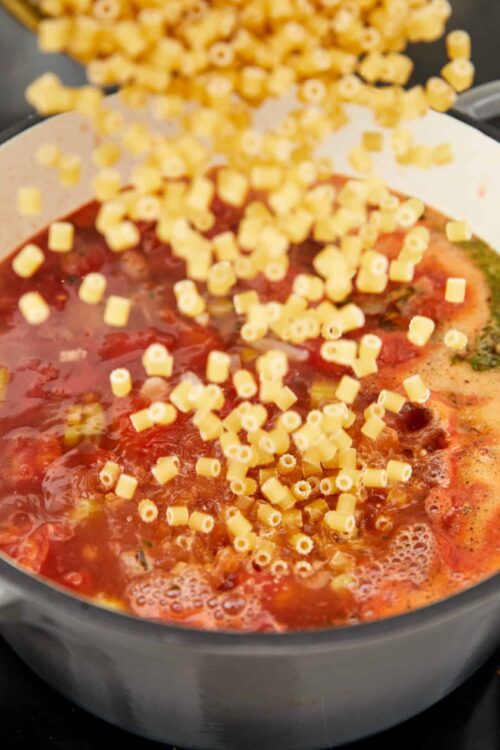 Shredded cheese melting into tomato sauce in a skillet for cheesy pasta dish.