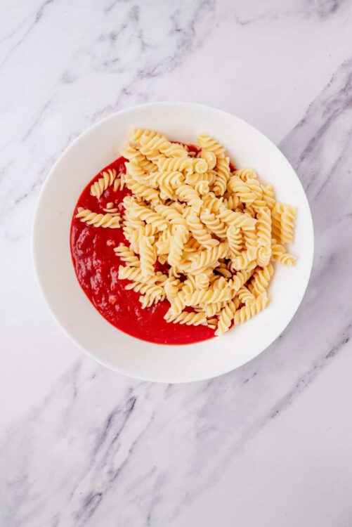 Creamy tomato sauce with cooked fusilli pasta in a white bowl, served on a marble countertop.