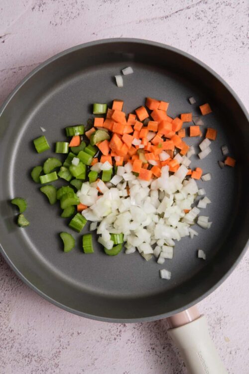 Chopped celery, carrots, and onions in a non-stick skillet for cooking.