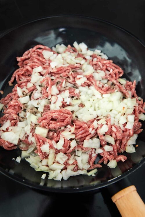 Ground beef and chopped onions cooking in a skillet.