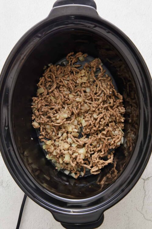 Ground beef and chopped onions in a slow cooker, ready for cooking or recipe preparation.