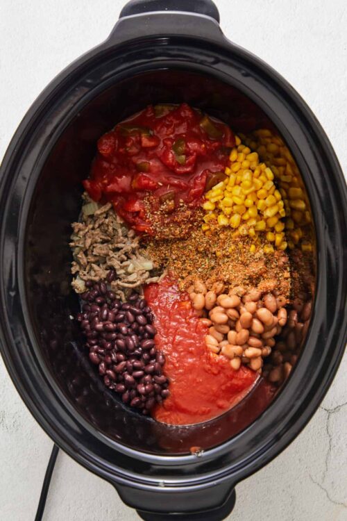 Crockpot with ground beef, black beans, corn, tomatoes, onions, and spices ready for chili recipe.