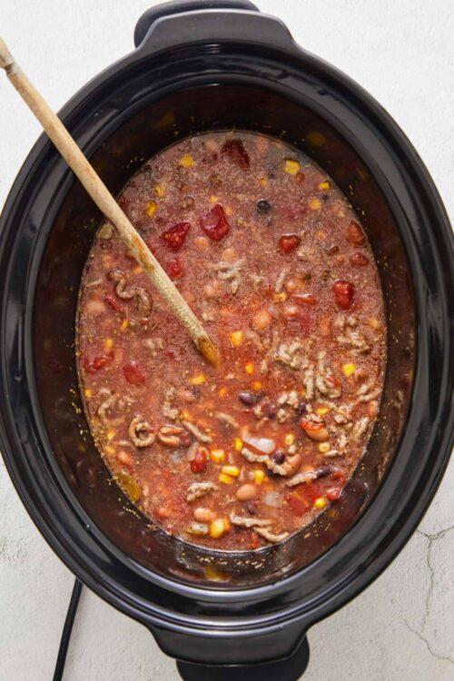Rich slow cooker chili with beans, corn, and ground meat in a black crockpot.