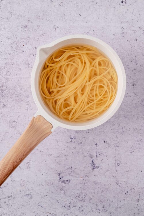 Cooked spaghetti pasta in a white bowl on kitchen counter, ready for recipes.