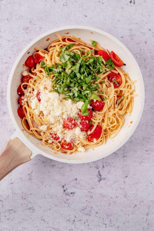 Fresh cherry tomato spaghetti with basil and parmesan cheese in a white skillet.