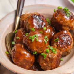 Savory meatballs with sauce and chopped green onions in a rustic bowl.
