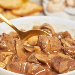 Savory beef stew with mushrooms and onions in a white bowl. Perfect comfort food for cozy family dinners.