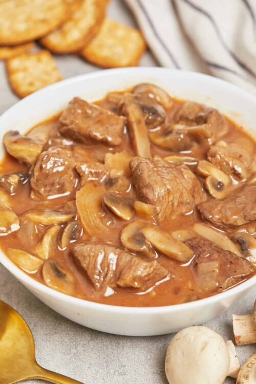Creamy beef and mushroom stew in a white bowl with side of golden toasted bread slices.