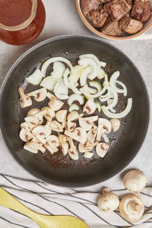 Sautéing sliced mushrooms and onions in a cast iron skillet.