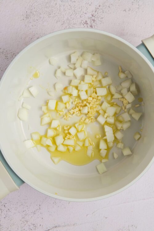 Diced onions and garlic in a white slow cooker, ready for cooking or making a savory dish.
