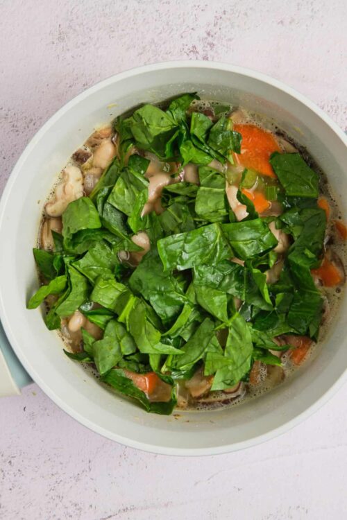 Fresh homemade chicken soup with carrots, greens, and herbs in a white bowl.