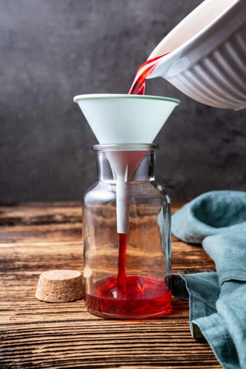Pouring red wine through a coffee filter into a glass bottle to clarify and improve taste.