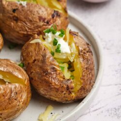 Baked potatoes with sour cream and chopped green onions on a white plate.