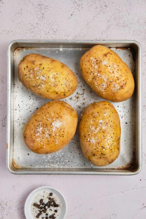 Juicy baked potatoes seasoned with salt and pepper on a baking sheet, ready for roasting.