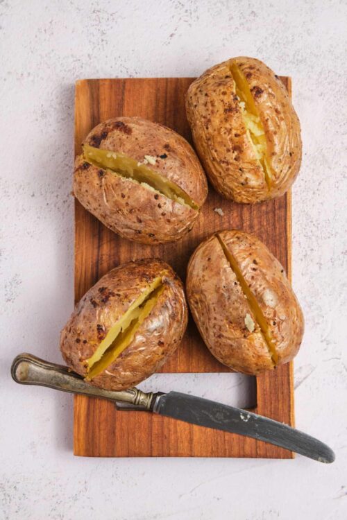 Baked sweet potatoes with slightly open skins on a wooden board with vintage knife.