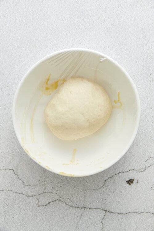 Soft bread dough ball in a white mixing bowl ready for baking.