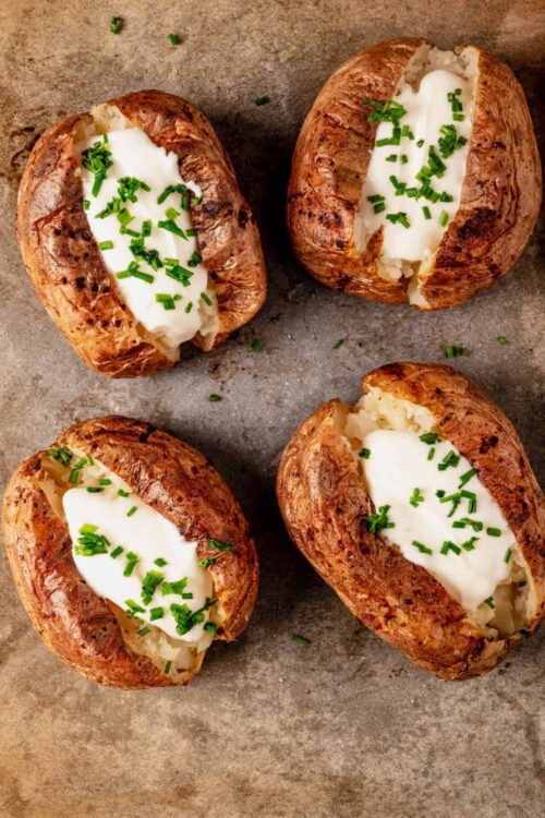 Baked potatoes topped with butter and chopped chives on a baking sheet.