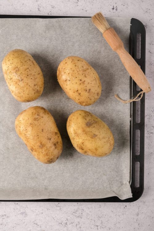 Raw potatoes on parchment paper with a scrub brush for baking or cooking.
