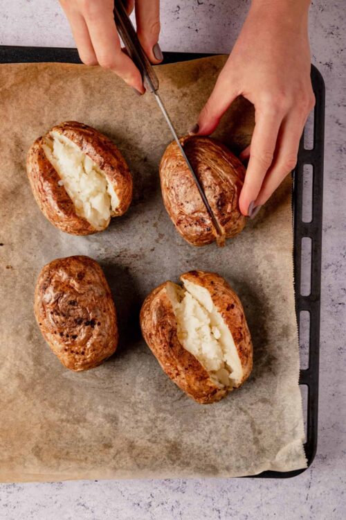 Roasted baked potatoes being sliced open, with creamy insides spilling out.
