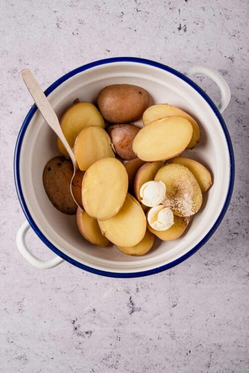 Boiled potatoes in a white and blue bowl with butter and seasonings.