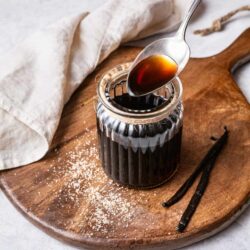 Rich vanilla extract in a glass jar on a rustic wooden board with vanilla beans.